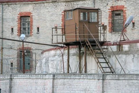 Old prison wall with barbed wire and observation tower behind it. Old pris... 写真素材