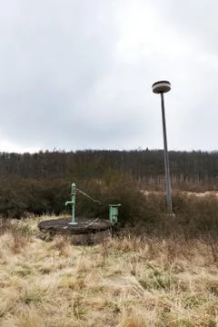 Old pump with leafless forest, water shortage scarcity concept 库存照片