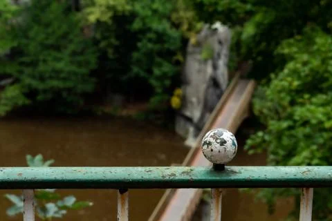 Old railing with a worn ball overlooking a serene river and lush greenery day Stock Photos