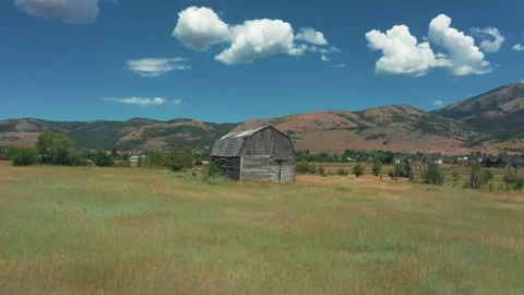 An old red barn set against the dramatic backdrop of majestic mountains veiled Stock Footage 255864124