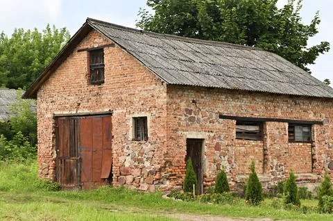 Old red brick barn standing on green grass field in rural village outdoors. 스톡 사진