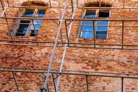 Old red brick building with weathered windows and construction scaffolding .. Stock Photos