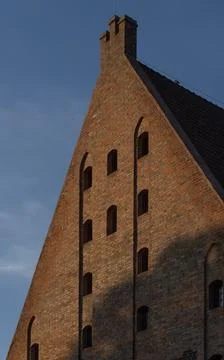 Old red brick gothic building facade against clear blue sky Stock Photos