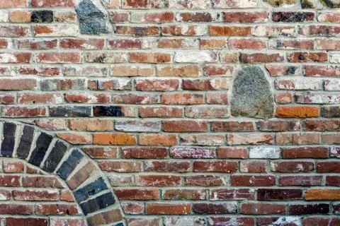 Old red brick wall with granite stones insertion, arch and blooming mallow, v 库存照片