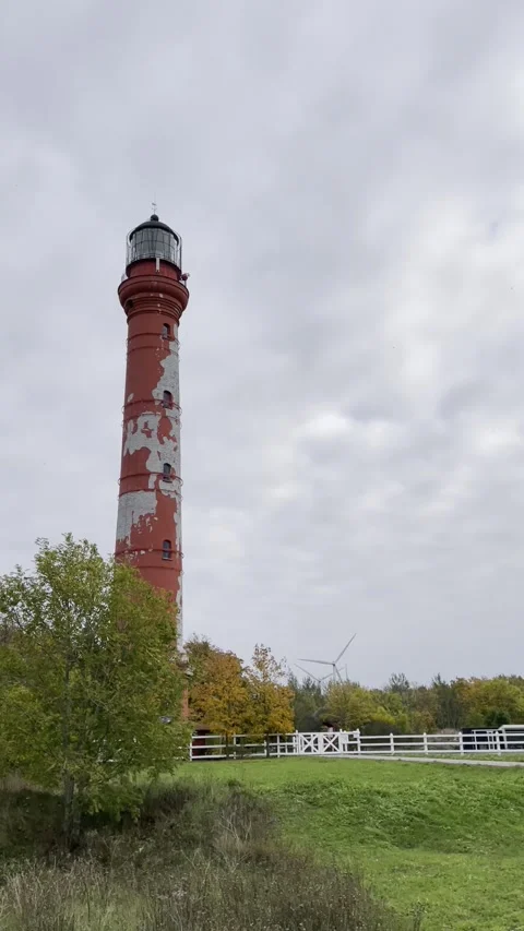 Old red lighthouse with peeling paint under cloudy sky Vídeo Stock 338403892