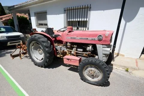 Old red tractor with plow attachment parked on a sunny village street near .. Stock Photos