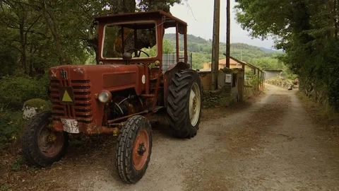 OLD RED TRACTOR IS STANDING ON THE SIDE OF A ROAD IN THE MIDDLE OF NATURE Stock Footage 209138932