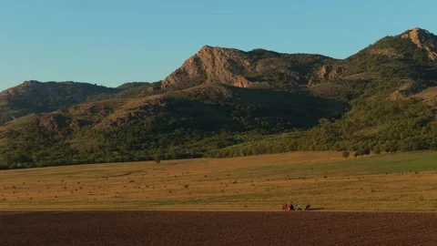 Old red tractor towing a trailer along a country road, surrounded by Stock Footage 294493753