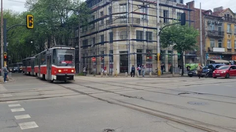 An old red tram leaves a stop and crosses an intersection in central Sofia Stock Footage 316136408