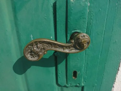 An old richly decorated brass door handle on the old wooden door painted green Stock Photos