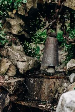 Old ritual bell hanging from rusty chain in stone arch surrounded by moss a.. Foto stock