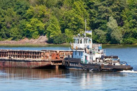 An old river tug pushes an empty barge ahead of itself along the river bank. Stock Photos
