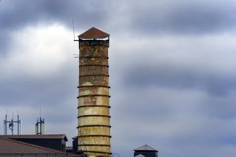An old round brick tower over the rooftops of houses and an overcast sky Stock Photos