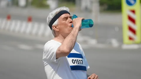 Old runner drink water at run marathon. Thirsty senior man. Elder thirst person. Stock Footage 308163563