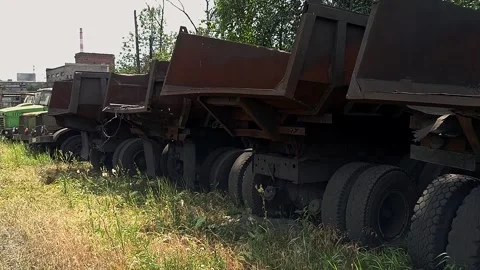 Old, rust-eaten trucks rest on a weed-choked wasteland Stock Footage 312152880