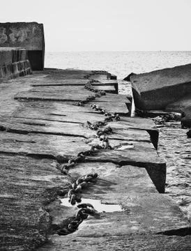 Old rusted chains lying on concrete pier with horizon of sea in background Stock Photos