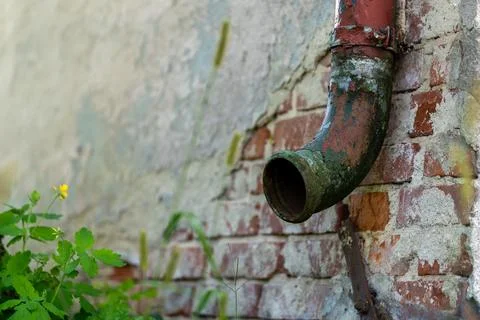 Old rusted gutter downpipe next to a damaged wall with falling plaster Fotos de archivo