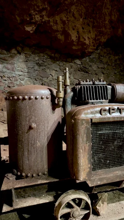 Old rusted mining engine and boiler sit on a wheeled cart in a stone tunnel as Stock Footage 345645310