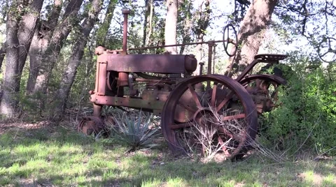 Old rusted tractor sitting in a field with trees grown around it Stock Footage 48984052