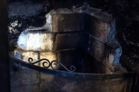 An old, rustic fireplace with dirty bricks and wrought iron fire screen Stock Photos