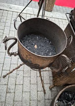 Old rustic iron cauldron filled with black charcoal ashes on a metal tripod.. Foto stock