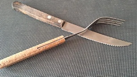 Old rustic kitchen fork and serrated steak knife crossed together Stock Photos