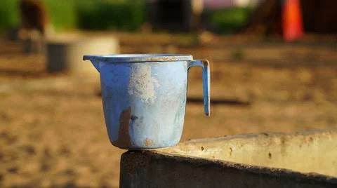 Old rustic plastic watering mug holding on rough column. Blue empty mug close Stock Photos