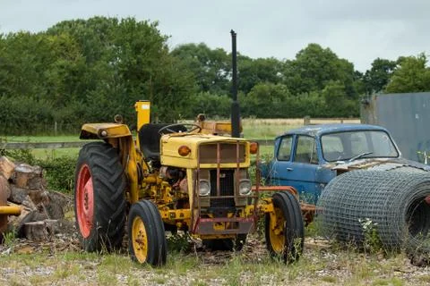 Old, rusting, yellow tractor on waste ground. Stock Photos