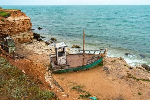 An old rusty abandoned boat is located on the seashore. Stock Photos