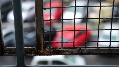 Old rusty balcony grate on background of blurred street car traffic and raining Stock Footage 160122437
