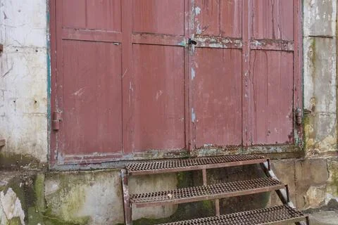 Old rusty brown gate. Peeling moldy plaster on the wall. Stock Photos