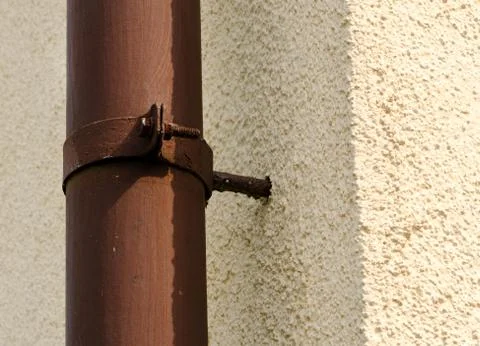 Old rusty brown gutter on the yellow wall. Stock Photos