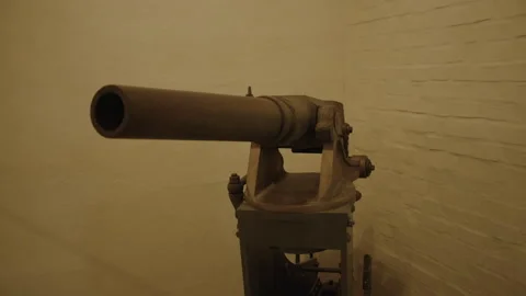 An old, rusty cannon sits mounted on a metal base against a brick wall.  Stock Footage 301033298