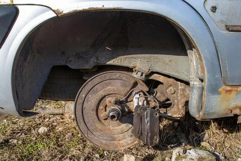 An old rusty car with a falling off wheel. Auto junk rusting on the side of t Stock Photos