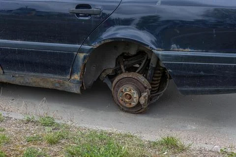 Old rusty car without rear wheel on the side of the road Stock Photos