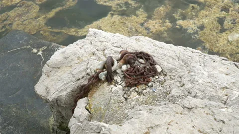 An old, rusty chain from an anchor chained to stone by the sea. Stock Footage 106569611