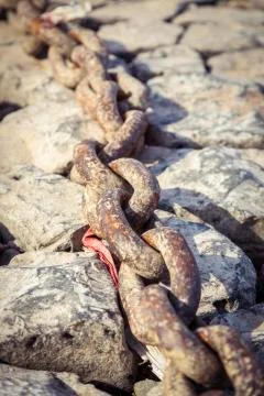 Old rusty chain on some rocks with light sepia color filter Stock Photos