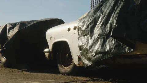 Old rusty classic car partially covered with a tarp in an outdoor junkyard. Stock Footage 322143081