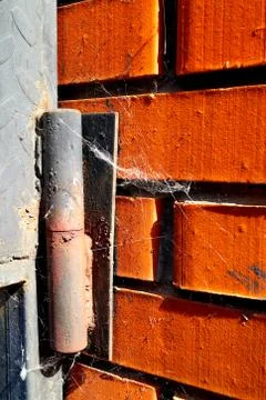 Old rusty door hinge with a spider web on a red brick wall. Stock Photos
