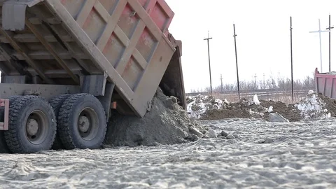 Old rusty dump truck brought frozen earth to winter construction site, unloading Stock Footage 115925292