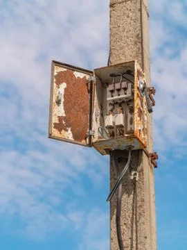 Old rusty electrical metering board on a concrete pillar with wires and fuses Stock Photos