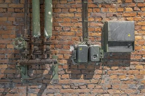 Old rusty electrical panel with buttons and wires and water pipes with taps o Stock-Fotos