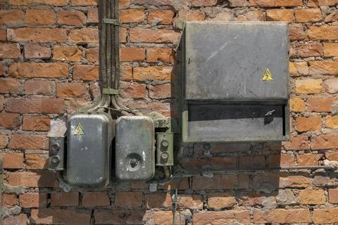 Old rusty electrical panel with buttons and wires on a ragged red brick wall  Foto stock
