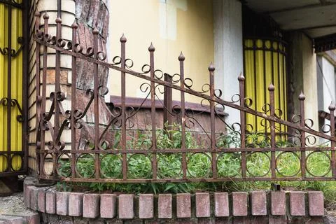 Old rusty fence of difficult shape near the building Stock Photos