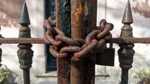 The old rusty gate is closed and wrapped with a thick steel chain with a lock Stock Photos