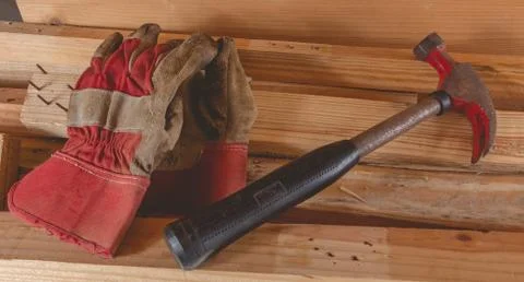 Old rusty hammer and construction gloves laid on wooden board Stock Photos