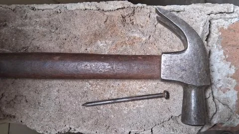 Old rusty hammer resting on cracked concrete surface. Vintage hand tool for Stock Photos
