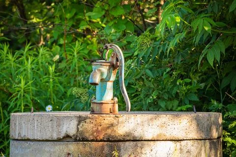 An old, rusty hand pump well in the forest. Still works and water still drink Stockfoto's