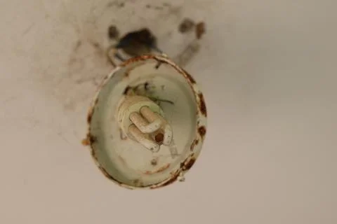 Old, rusty light fixture with a fluorescent bulb on a dirty ceiling Stock Photos