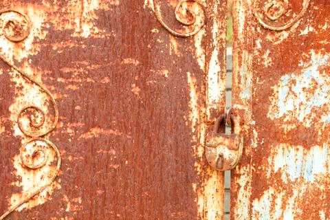 An old rusty lock connects a rusty gate. Rust on old metal sheet texture. Stock Photos